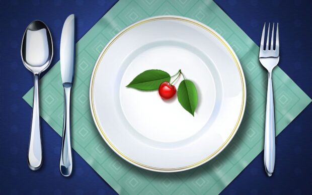 White plate with a cherry and green leaves on a teal napkin with spoon knife and fork laid out