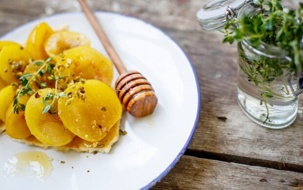 Yellow sliced fruit on a plate with honey dipper and herbs on a wooden table