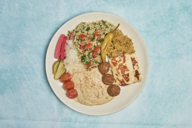 A plate of Mediterranean food with falafel tomato and grilled cheese on a blue surface