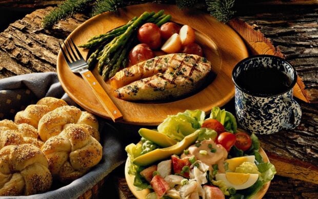 Grilled fish and fresh vegetables served on a wooden plate with bread and coffee on a rustic table