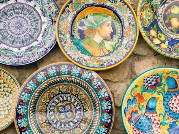 Colorful ceramic plate featuring detailed patterns and a human figure profile on a stone wall background