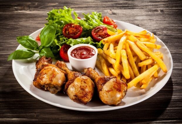Grilled chicken drumsticks served with french fries and fresh salad on a plate