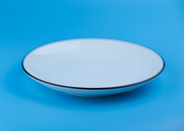 A white plate with a black rim on a blue surface displayed in high definition