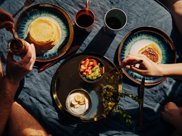 Blue ceramic plate holding pancakes with chocolate spread and fruit on a tray viewed from above
