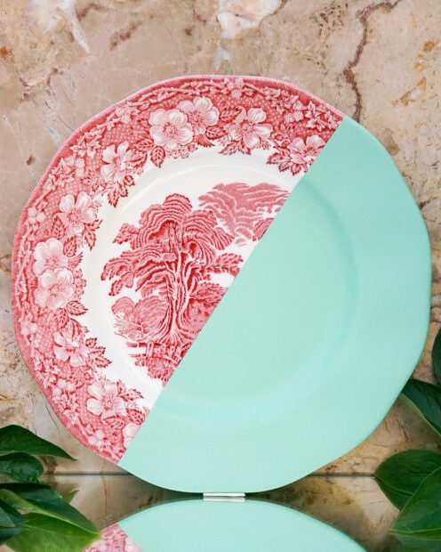 Half of a decorative vintage plate with red floral pattern and half solid mint color on a marble surface