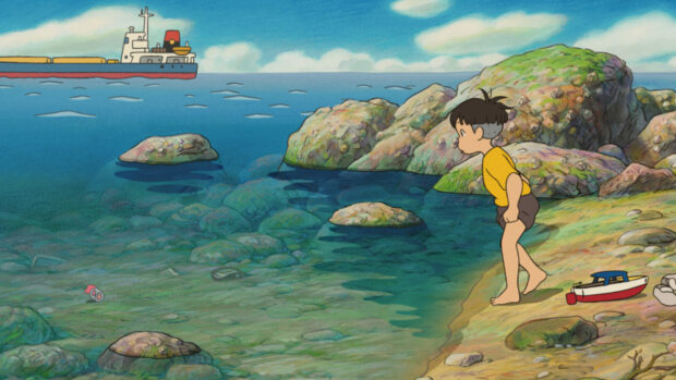 A boy stands near clear water and rocks by the sea in a Ponyo scene