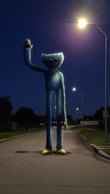 Huggy Wuggy stands on a dark street waving under streetlights at night