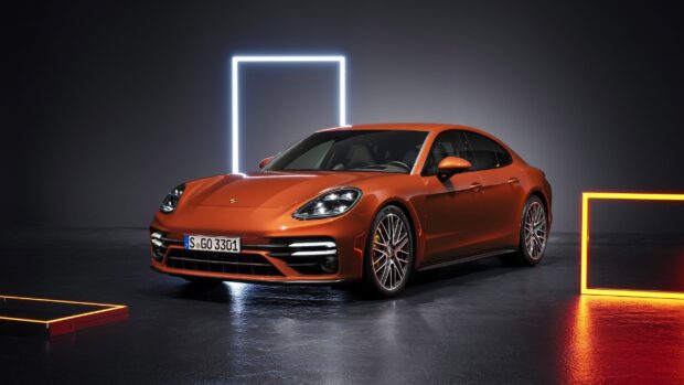 Orange Porsche Panamera car parked in a dark room with glowing neon frames