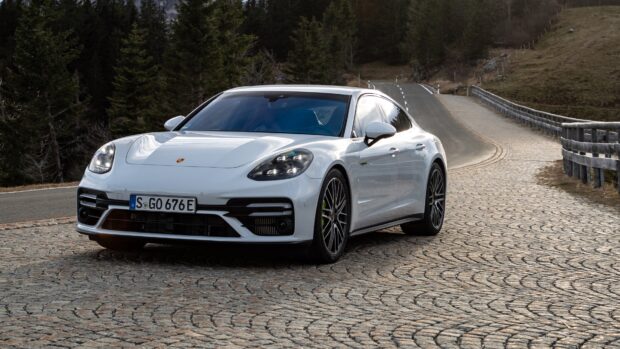 White Porsche Panamera parked on a cobblestone road near forest trees