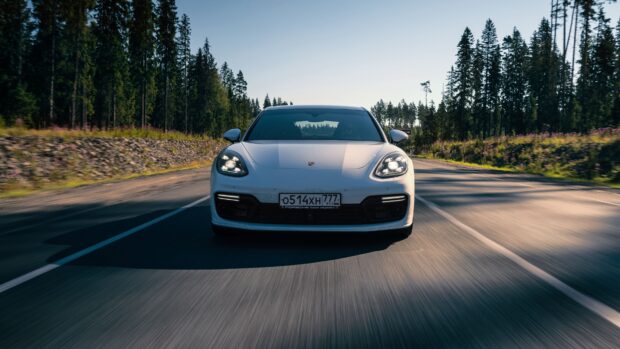 A white Porsche Panamera moving fast on a forest road during daylight