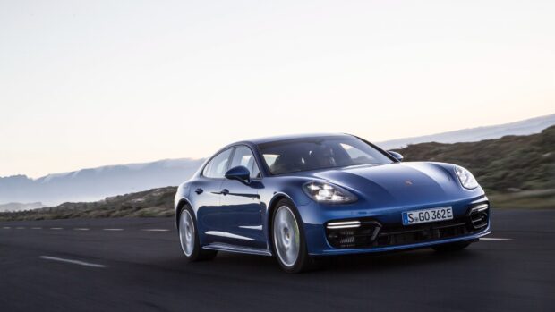 Blue Porsche Panamera driving fast on the road during sunset with mountain background