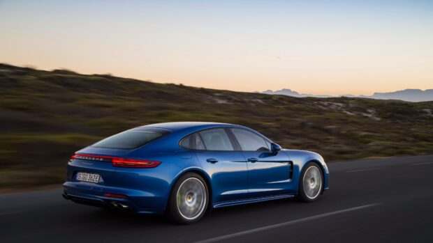 Blue Porsche Panamera driving on a road at sunset with mountains in the background
