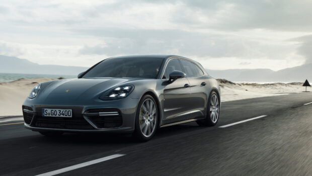 Grey Porsche Panamera driving on a coastal road with mountains in the background