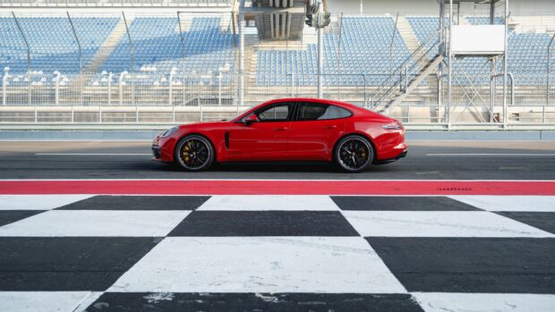 Red Porsche Panamera parked on a racetrack with empty blue stadium seats in the background