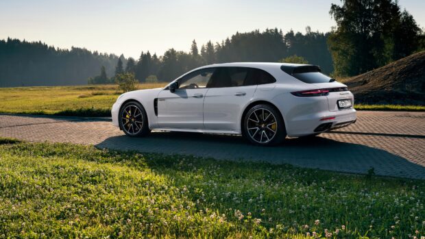 White Porsche Panamera parked on a paved area near a green field and forest in the background