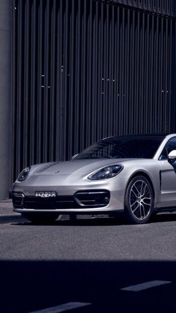 A silver Porsche Panamera parked on the street with a black vertical fence in the background
