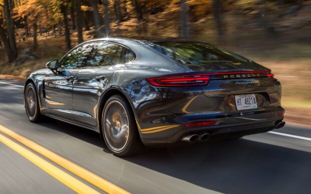 Black Porsche Panamera driving fast on a forest road in autumn