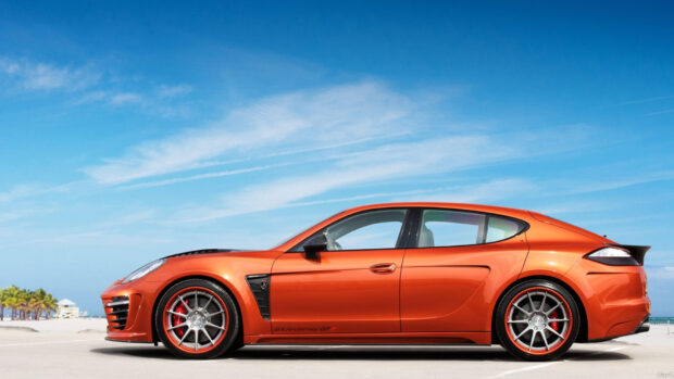 Orange Porsche Panamera sports car on the beach under a blue sky