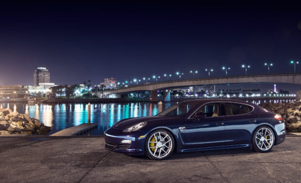 Porsche Panamera luxury car parked near waterfront at night with city lights in background
