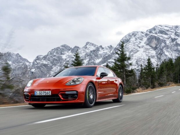 Red Porsche Panamera driving fast on a mountain road with snowy peaks in the background