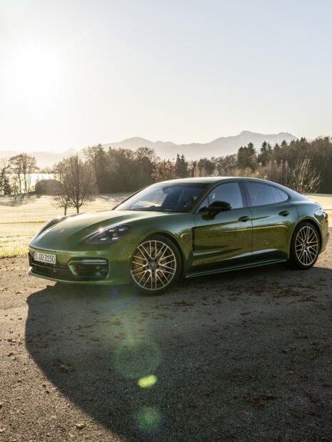 Green Porsche Panamera parked on a scenic roadside with mountains in the background sunlight illuminating the car