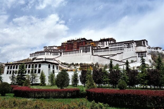 The Potala Palace standing majestically with lush greenery and a bright sky in the background