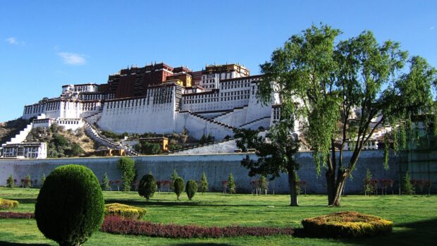 The Potala Palace surrounded by green trees and gardens under a clear blue sky