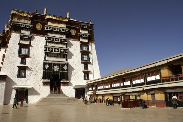 The main entrance of Potala Palace with traditional decorations and people walking around under clear blue sky