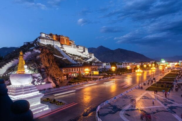 Potala Palace lit up at night overlooking the busy street and surrounding mountains