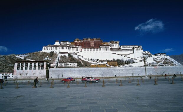 Potala Palace seen from the square under a clear blue sky with cars and cyclists passing by