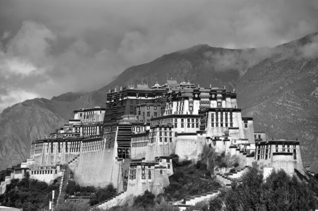 The historic Potala Palace stands prominently against mountain clouds in a black and white scene