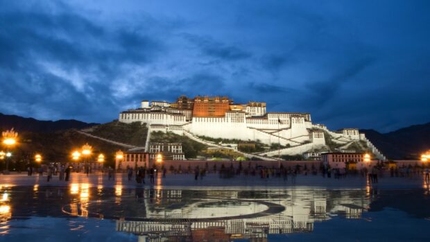 The Potala Palace is illuminated at night with its reflection visible on the wet ground