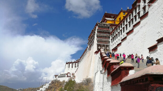 The Potala Palace with tourists climbing stairs under a blue sky and white clouds