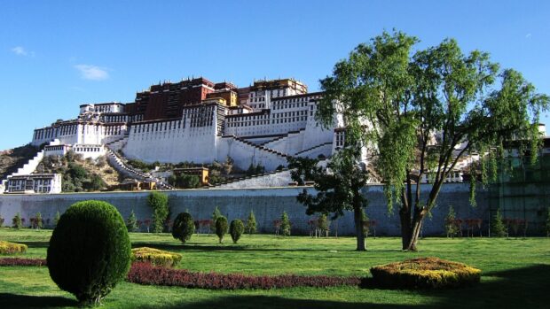 A majestic view of Potala Palace surrounded by green gardens under a clear blue sky