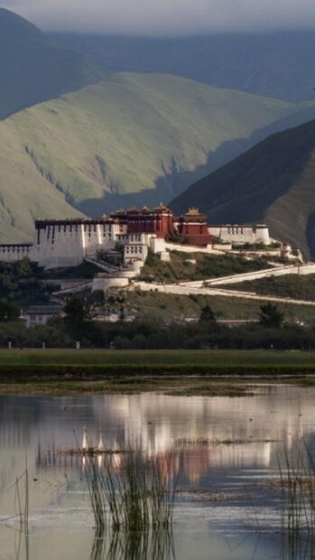 Potala Palace is reflected on the calm water with mountains in the background