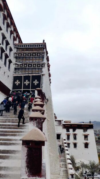 Visitors climbing the historic stairs of Potala Palace in Tibet on a cloudy day