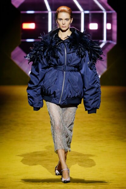 Female model wearing a Prada jacket with feather details on the runway