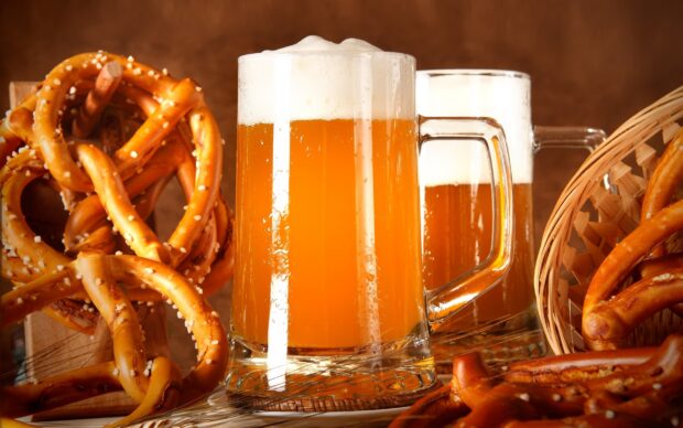Soft pretzel twisted snacks with coarse salt next to two frothy beer mugs