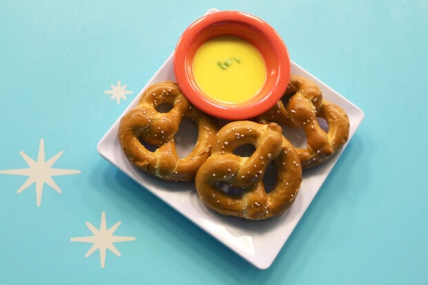 Fresh pretzel with a bowl of cheese sauce on a white plate on a blue table