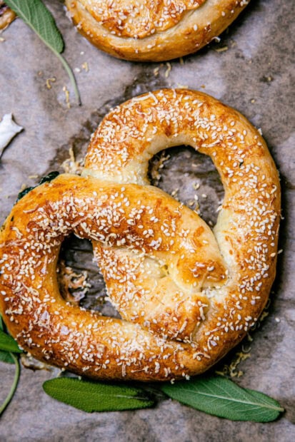 Freshly baked pretzel topped with sesame seeds and herbs on parchment paper