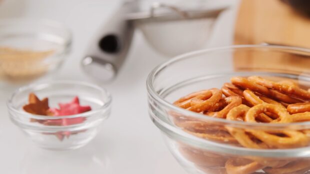 A glass bowl filled with salted pretzels on a kitchen counter with baking ingredients in the background