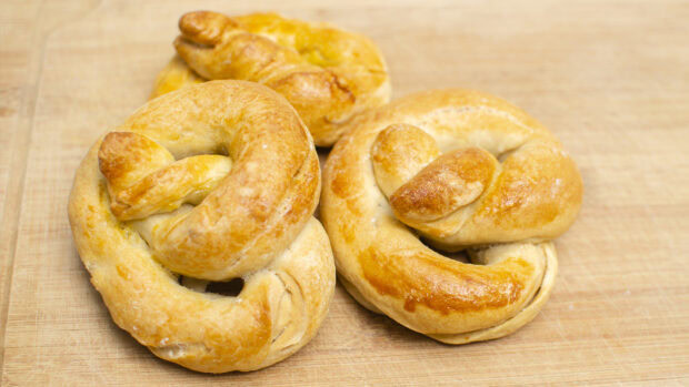 Three fresh pretzel bread rolls on a wooden surface showing golden crust