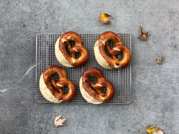 Four freshly baked pretzels cooling on a wire rack with autumn leaves around