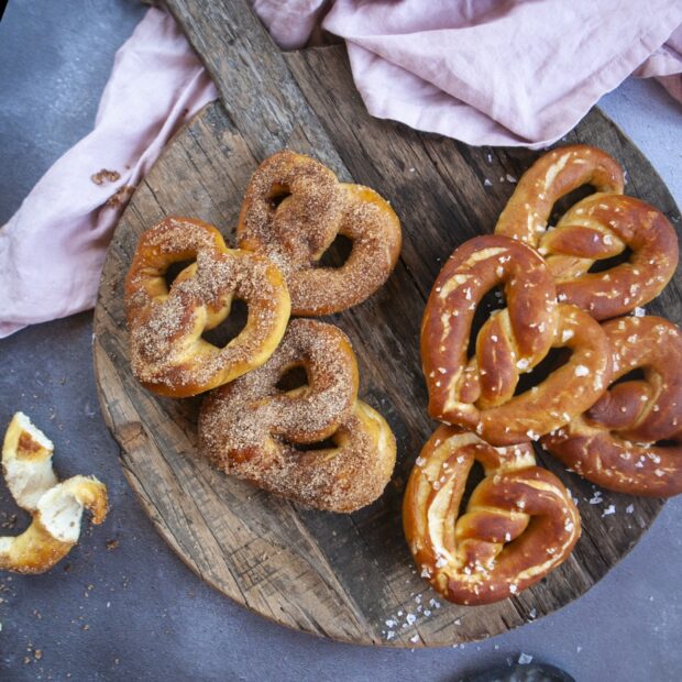 Fresh baked pretzel topped with coarse salt and cinnamon sugar on a rustic wooden board