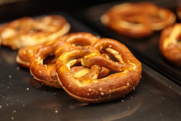 Freshly baked pretzel with coarse salt on a dark tray in a closeup view