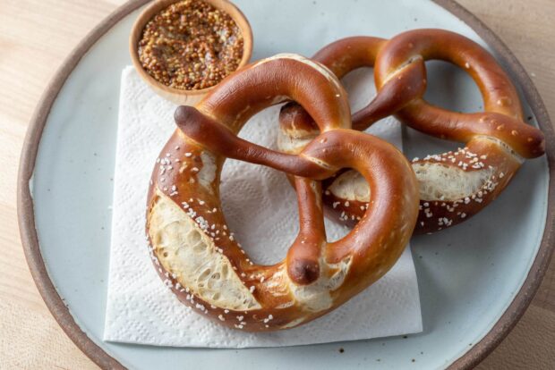 Two freshly baked pretzels sprinkled with salt served on a plate with mustard