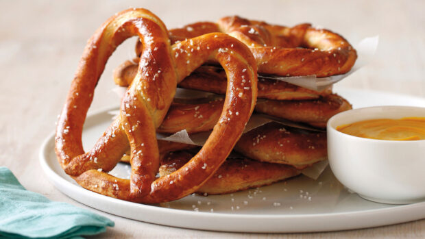 A close up of a large salt sprinkled pretzel on a plate with a bowl of mustard sauce