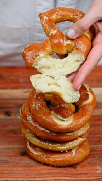 Fresh pretzel being torn by hand showing its soft texture on a wooden table