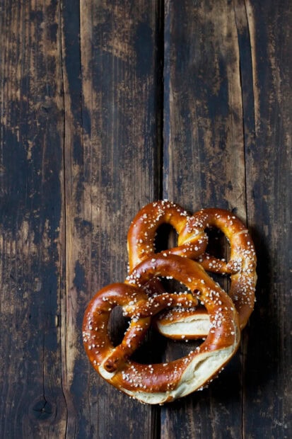 Two salty pretzels stacked on a rustic wooden surface with coarse salt sprinkled on top