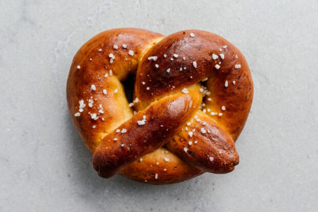 A close up of a salted golden brown pretzel on a gray surface